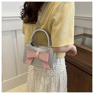 Silver mini square bag with a pink bow accent shown on a model in a lifestyle setting
