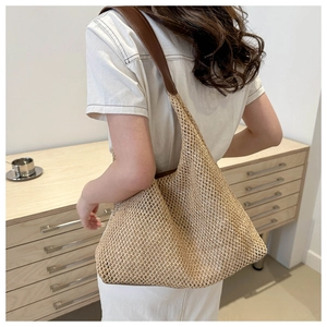 Detail of hand-woven straw hobo bag with brown leather strap on a model shoulder