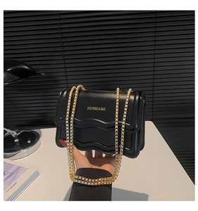 Close-up of black crossbody bag with wave edges and gold chain strap detail
