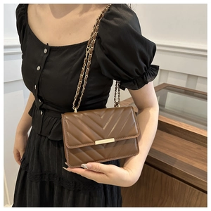Nahaufnahme der braunen Stepptasche mit goldener Schließe und Kettengurt an einem Model