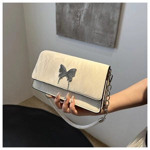 Close-up of cream quilted bag featuring a silver butterfly buckle and textured leather