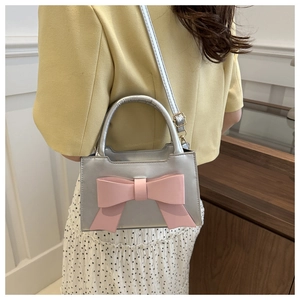 Detail of silver mini crossbody bag featuring a large pink bow on a metallic surface