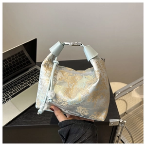 Détail d'un sac en satin bleu clair avec motifs de pins en jacquard doré et fermoir métal