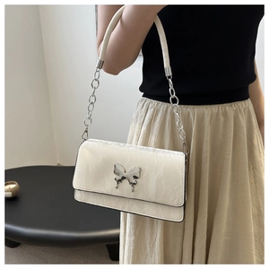 Close-up of beige shoulder bag featuring silver metallic butterfly buckle and chain strap
