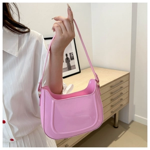 Detail of pink patent leather shoulder bag with glossy finish and curved saddle design