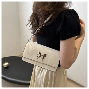 Detail view of cream shoulder bag with silver butterfly buckle and chain strap