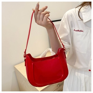 Close-up of red patent leather crescent bag with adjustable strap and shiny finish