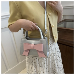 Detail of silver crossbody bag with pink bow accessory worn by a model in casual outfit