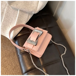Close-up of pink mini crossbody bag with silver buckle and chain on plaid seat