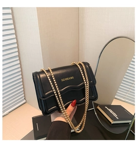 Close-up of black leather crossbody bag with wavy flap design and gold chain strap