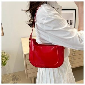 Close-up of bright red patent leather crescent bag with sleek glossy surface and slim strap
