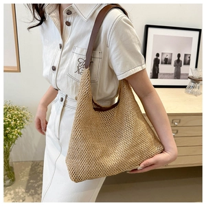Detail of woven straw tote bag with brown leather strap worn over shoulder on dress