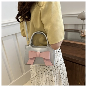 Detail of silver metallic handbag with a large pink bow shown on a shoulder strap