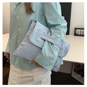 Detail of light blue clutch with wrinkled paper texture and wide strap on the flap