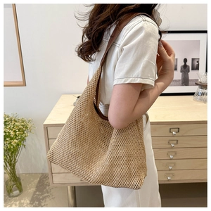 Detail of woven straw tote bag with brown leather strap worn by a model in interior