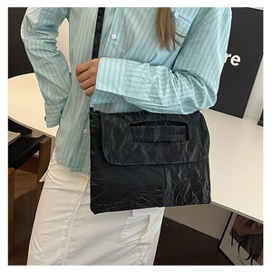 Close-up of black pleated texture shoulder bag with cutout handle and metal strap attachment