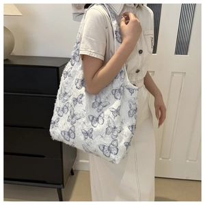 Close-up of plush white tote bag featuring blue butterfly patterns and fuzzy texture