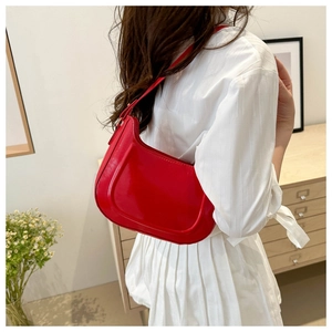 Close-up of a glossy red patent leather crescent shoulder bag worn on model's shoulder