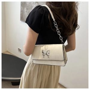 Close-up of cream underarm bag with silver butterfly buckle and leather chain strap