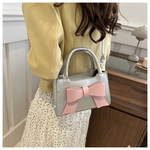 Detailed view of silver handbag with a large pink bow, showing strap and handle