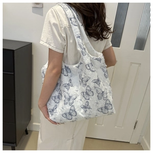 Close-up of white canvas tote bag featuring blue butterfly patterns and fringe texture