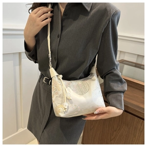 Détail du sac beige avec motifs floraux traditionnels et pendentif à pompon perlé