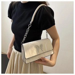 Detail of creamy white crossbody bag with silver butterfly clasp and chain strap on model
