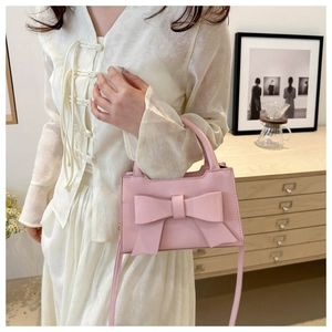 Detailed close-up of pink bow handbag with rounded handle and fine synthetic leather texture
