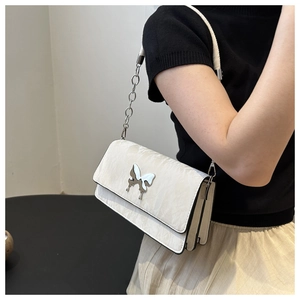 Close-up of cream crossbody bag featuring a silver butterfly clasp and chain strap