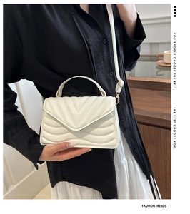 Detail of white V-quilted faux leather handbag with golden hardware and top handle