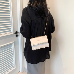 Minimalist beige crossbody bag with wavy edge flap and elegant gold chain strap
