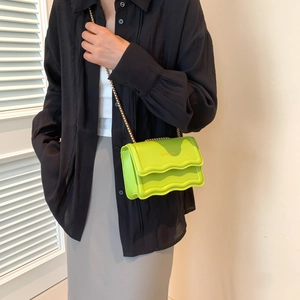 Neon green scalloped crossbody bag with gold lettering and metal chain strap on model