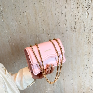 Chic pink wavy edge crossbody bag with gold chain strap on a stone background