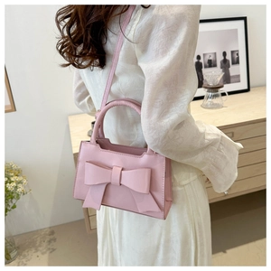 Detail of pink bow-knot handbag with rounded handle shown in minimalist interior setting