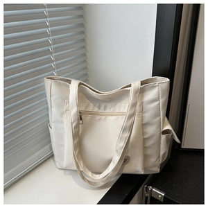 Detail of white canvas tote bag showing front zipper pocket and side storage pocket