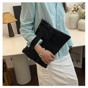 Close-up of black envelope clutch bag featuring detailed pleated texture and flap closure