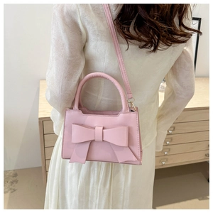 Model wearing a pink bow crossbody bag over a white dress in a minimalist room