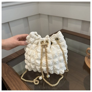 Dettaglio della borsa a secchiello bianca con texture a bolle e catena dorata