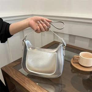 Modern metallic silver handbag with gold hardware displayed on a wooden table