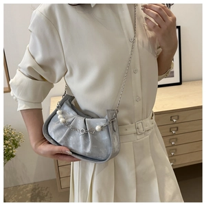 Detail of silver pleated cloud bag with pearl chain strap worn by a female model