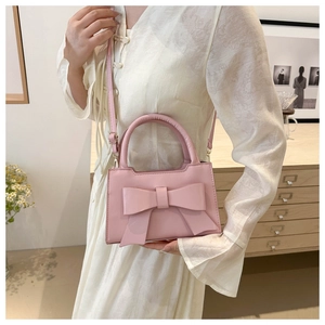 Pink crossbody bag with a large bow detail and top handle shown in a lifestyle setting