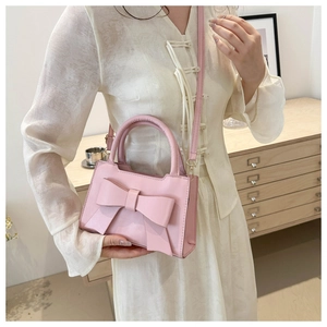 Detail of light pink crossbody bag with large bow decor and smooth faux leather finish