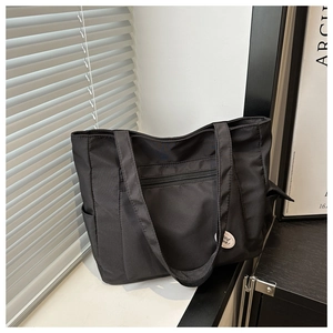 Detail of durable black nylon tote bag featuring front zipper pocket and side pocket