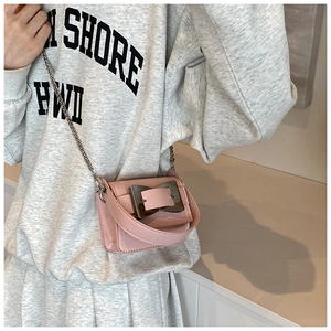 Close-up of pink chain bag with a gold buckle worn by a model as a crossbody bag
