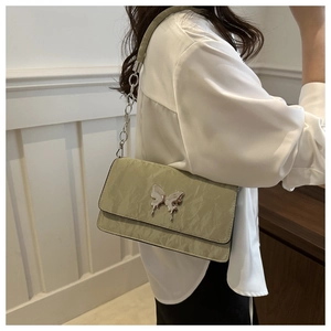 Detail of sage green quilted crossbody bag featuring a silver metal butterfly ornament