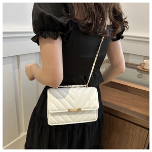 Detail einer weißen Stepptasche mit goldener Kette auf einem schwarzen Kleid