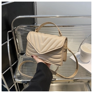 Close-up of beige quilted crossbody bag with classic V-shaped stitching and flap closure