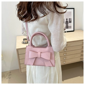 Pink bow handbag with adjustable strap shown in a stylish lifestyle scene