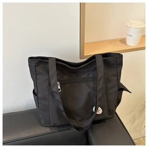Close-up of black nylon tote bag featuring front zipper pocket and Good Luck embroidery