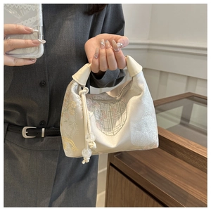 Détail du sac en satin beige avec broderie florale et breloque à pompon perlé chic